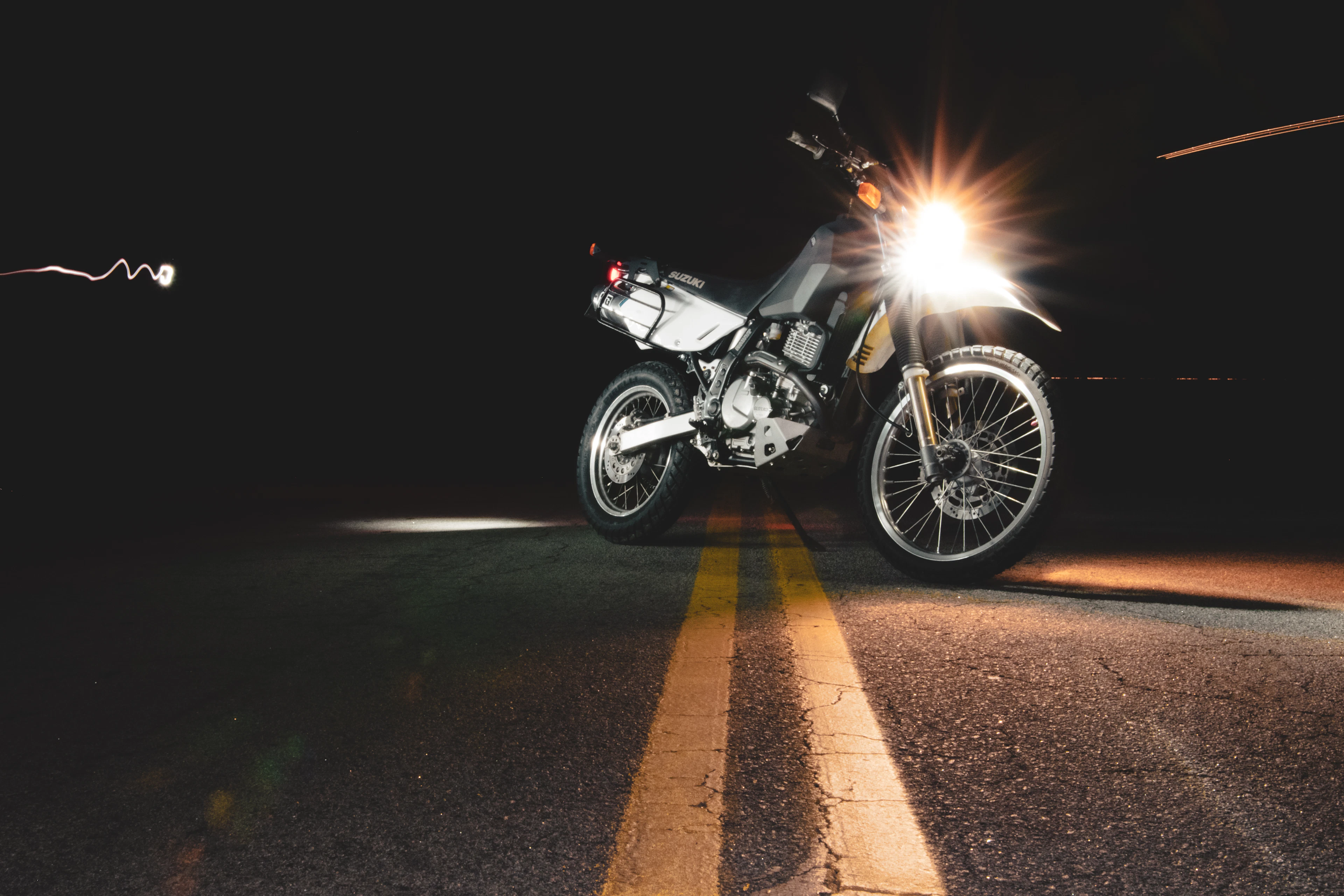 A dual-sport motorcycle at night, headlight on, on a road with yellow centre lines