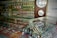 A display case filled with various types of wristwatches, organized with metal bands and different colors. Wall clocks are mounted on the wall behind the case, along with a range of colorful alarm clocks arranged in rows. Brand names like SEIKO, RADO, and CITIZEN are visible, suggesting a retail setting for timepieces.