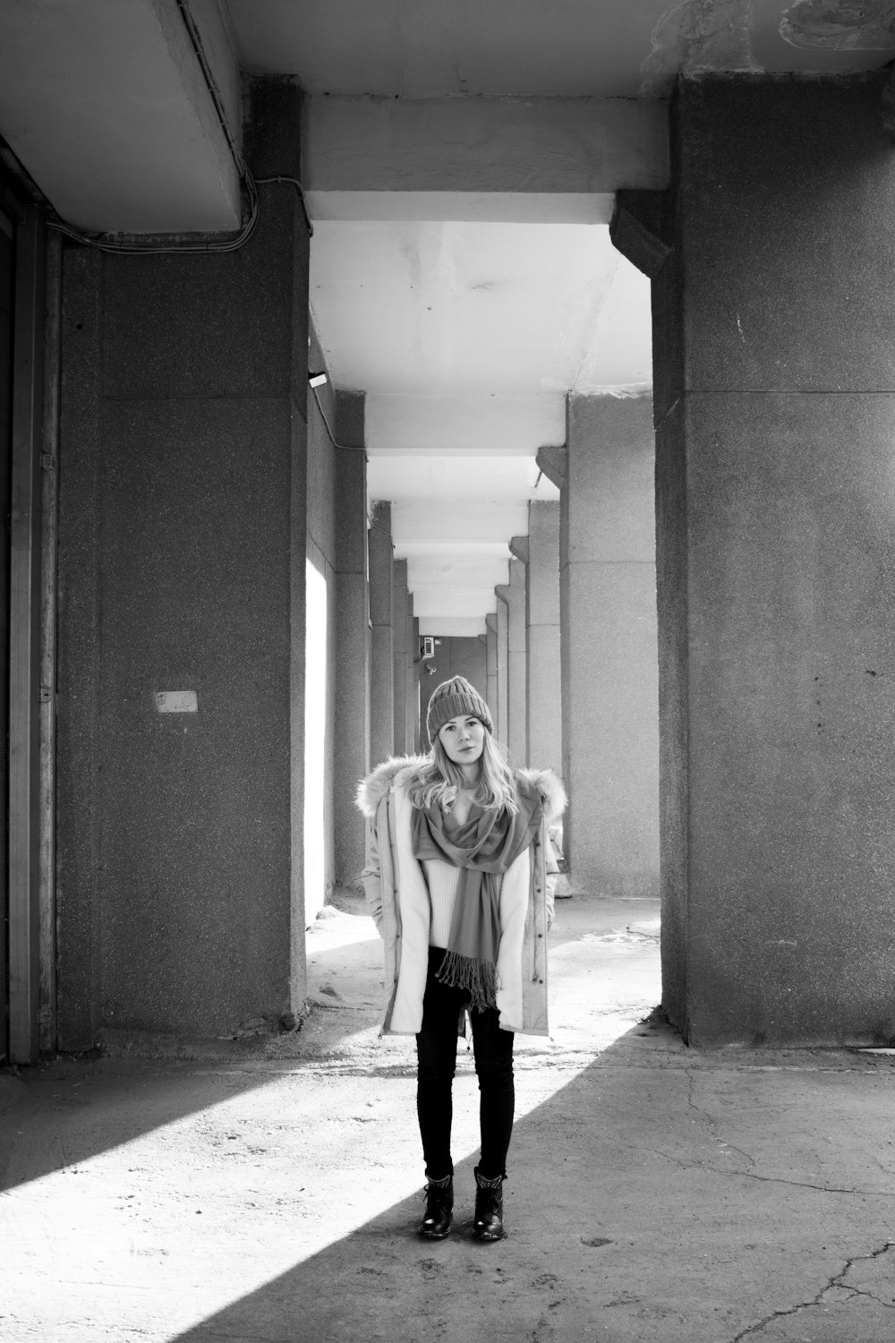 grayscale photography of woman standing near column