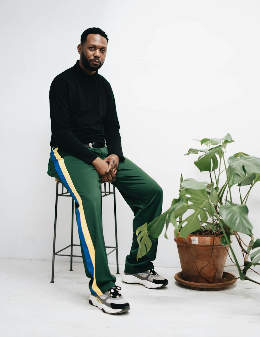 man sitting on black stool beside swiss cheese plant