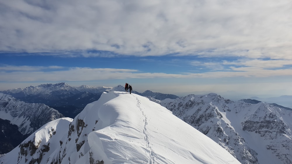 silhouette de personne au sommet d’une montagne enneigée sous un ciel nuageux blanc pendant la journée