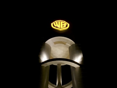 A large, illuminated sign featuring the letters 'WB' is prominently displayed against a dark night sky. The sign is positioned on a modern, cylindrical structure with smooth curves and is highlighted by bright lighting.