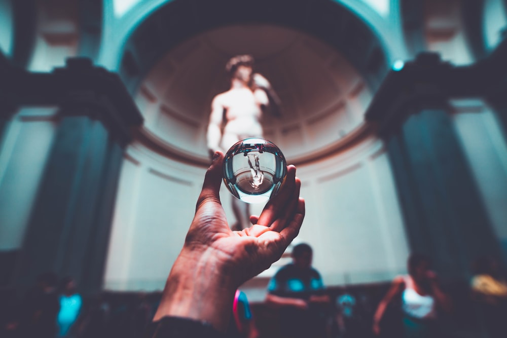 person holding clear ball near the statue