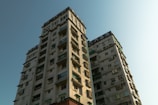 Two residential high-rise buildings with multiple balconies and windows. The structures exhibit a modern architectural style with a light-colored exterior.