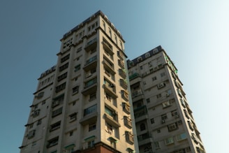 Two residential high-rise buildings with multiple balconies and windows. The structures exhibit a modern architectural style with a light-colored exterior.