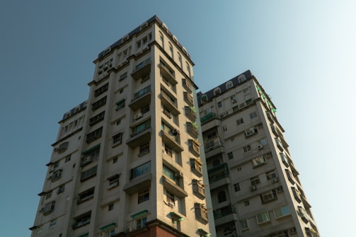 Two residential high-rise buildings with multiple balconies and windows. The structures exhibit a modern architectural style with a light-colored exterior.