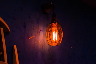 A warm pendant lamp casting soft light over a rustic wooden table in a cozy African-style cafe with thatch roof.
