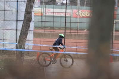 Close-up of a child tightening a bright orange helmet strap before riding.