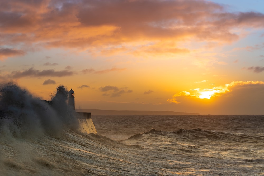 lighthouse beside shore with sunset background