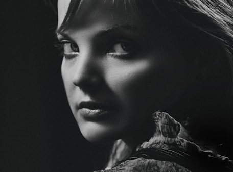 A striking black-and-white portrait with sharp contrasts, capturing an intense gaze in a minimalist dark setting