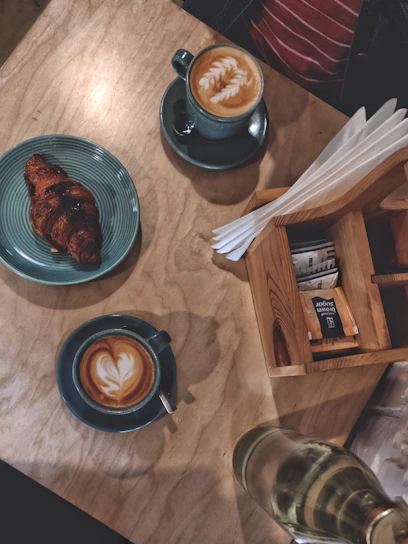 A rustic wooden table set with a steaming cup of espresso and a flaky croissant dusted with powdered sugar.