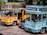 Two colorful tourist buses are parked side by side with visible branding for the Bandung city tour, one in a bright yellow color and the other in turquoise. A black car is partially visible between the buses. The scene is set outdoors with trees providing shade in the background.