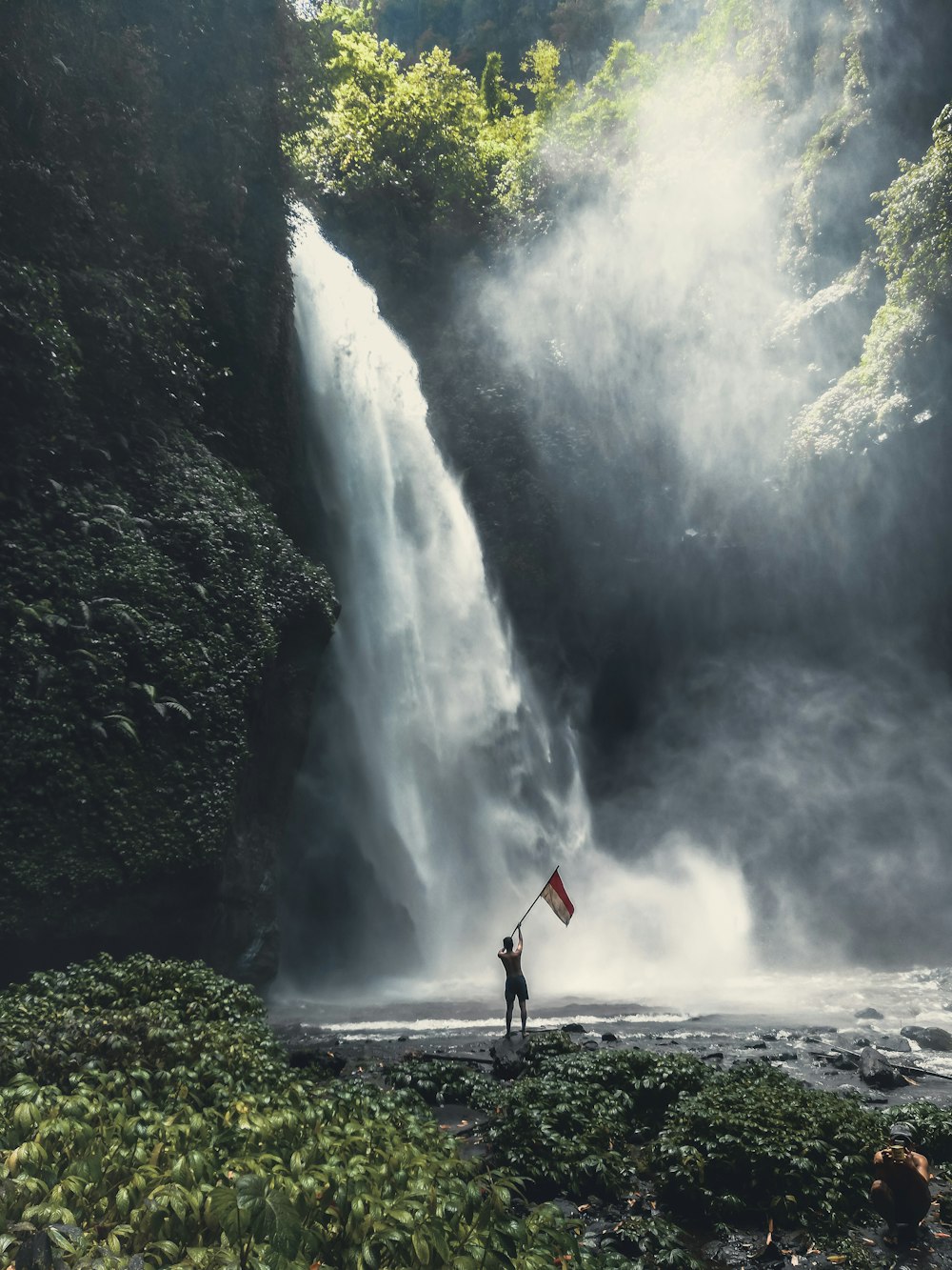 person holding flag standing near waterfalls