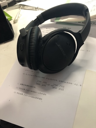 Close-up of headphones resting on a desk beside an open book and a laptop.