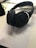 On a desk lies a pair of black over-ear headphones resting on a paper with mathematical text. Nearby, there are open books, part of a smartphone, and writing instruments, suggesting a study or work environment.