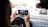 Person holding a smartphone while sitting in the driver's seat of a car, taking a photo or video of traffic ahead.
