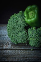 A close-up of fresh broccoli and a green bell pepper placed on a rustic wooden surface.