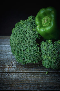 A close-up of fresh green vegetables and fruits laid out on a rustic wooden table.