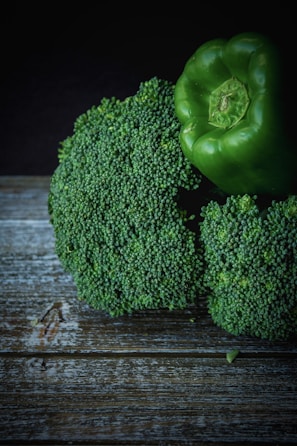 A close-up of fresh broccoli and a green bell pepper placed on a rustic wooden surface.