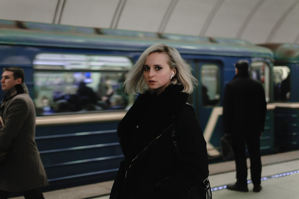 woman wearing black coat near the blue train
