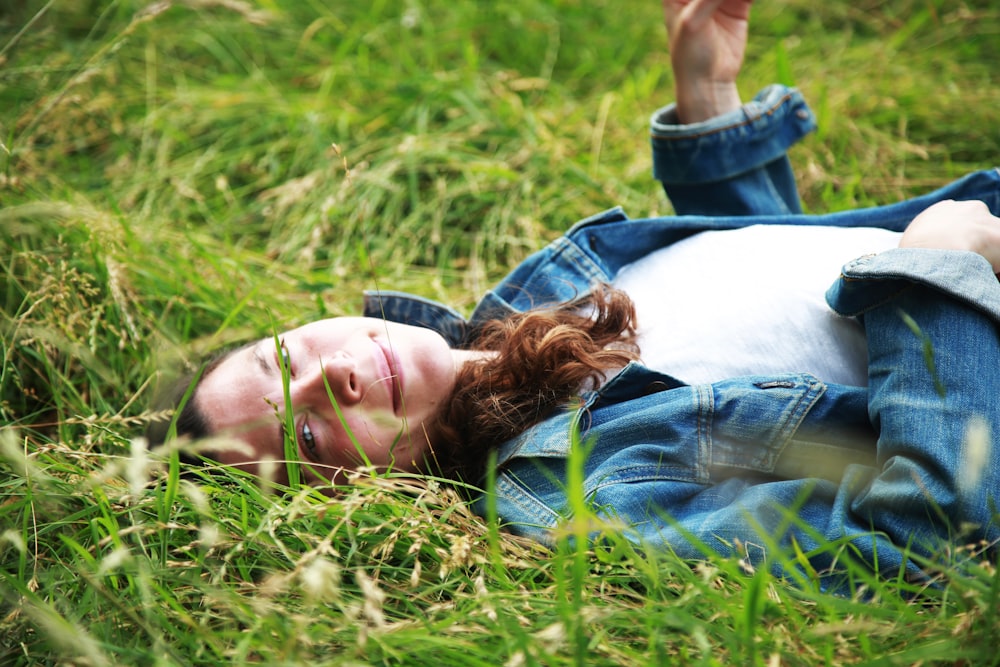 mulher na jaqueta jeans azul deitada na grama