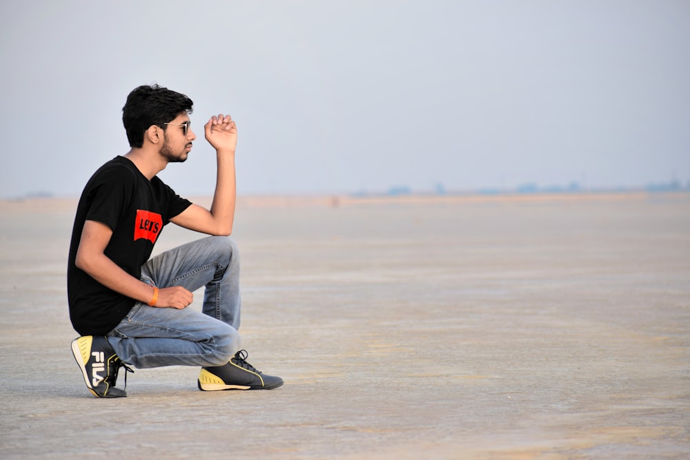 man in black Levis crew-neck T-shirt sitting on desert