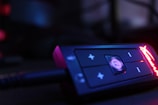A close-up view of an electronic device showcasing a control panel with buttons and LED lighting. The device is mostly black with prominent plus and minus buttons, and a glowing red brand logo is visible on the right side.