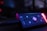 A close-up view of an electronic device showcasing a control panel with buttons and LED lighting. The device is mostly black with prominent plus and minus buttons, and a glowing red brand logo is visible on the right side.