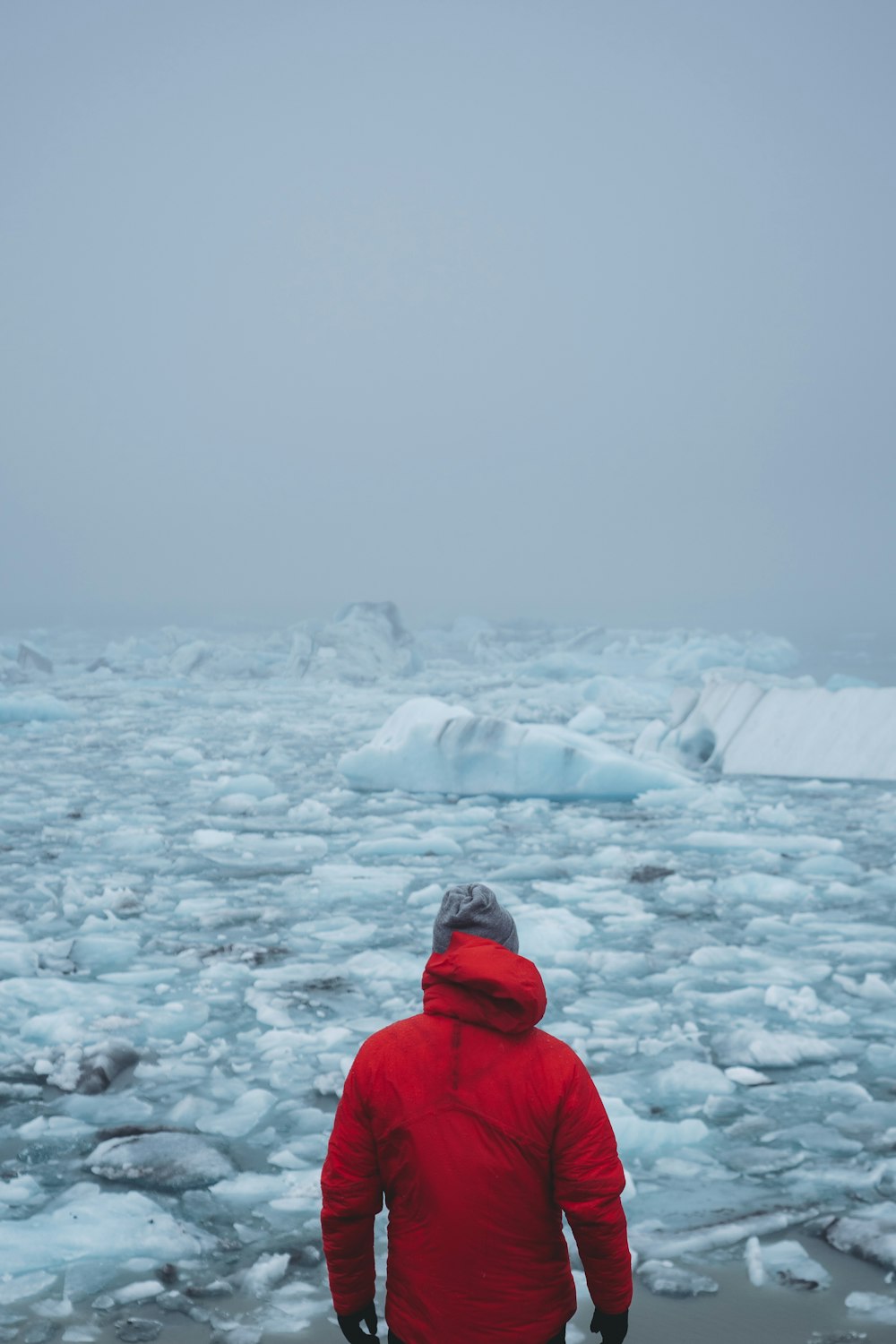 Hombre con abrigo rojo de pie frente al hielo flotante