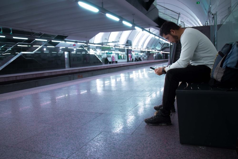 Uomo che si siede mentre usa lo smartphone nella stazione ferroviaria