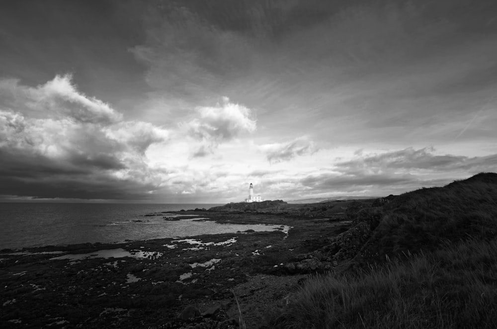 grayscale photography of lighthouse beside body of water