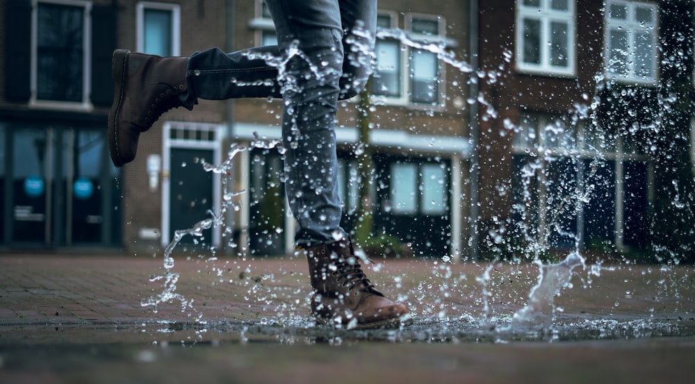person in gray jeans and brown boots walking on water puddle