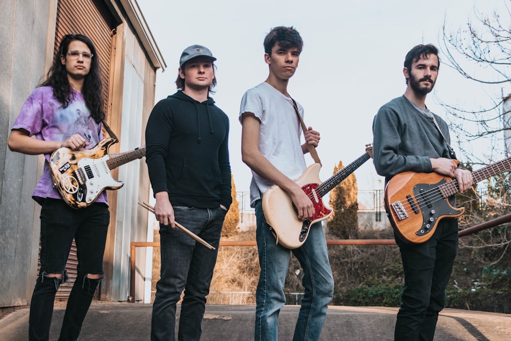 four person holding musical instruments standing near brown metal door