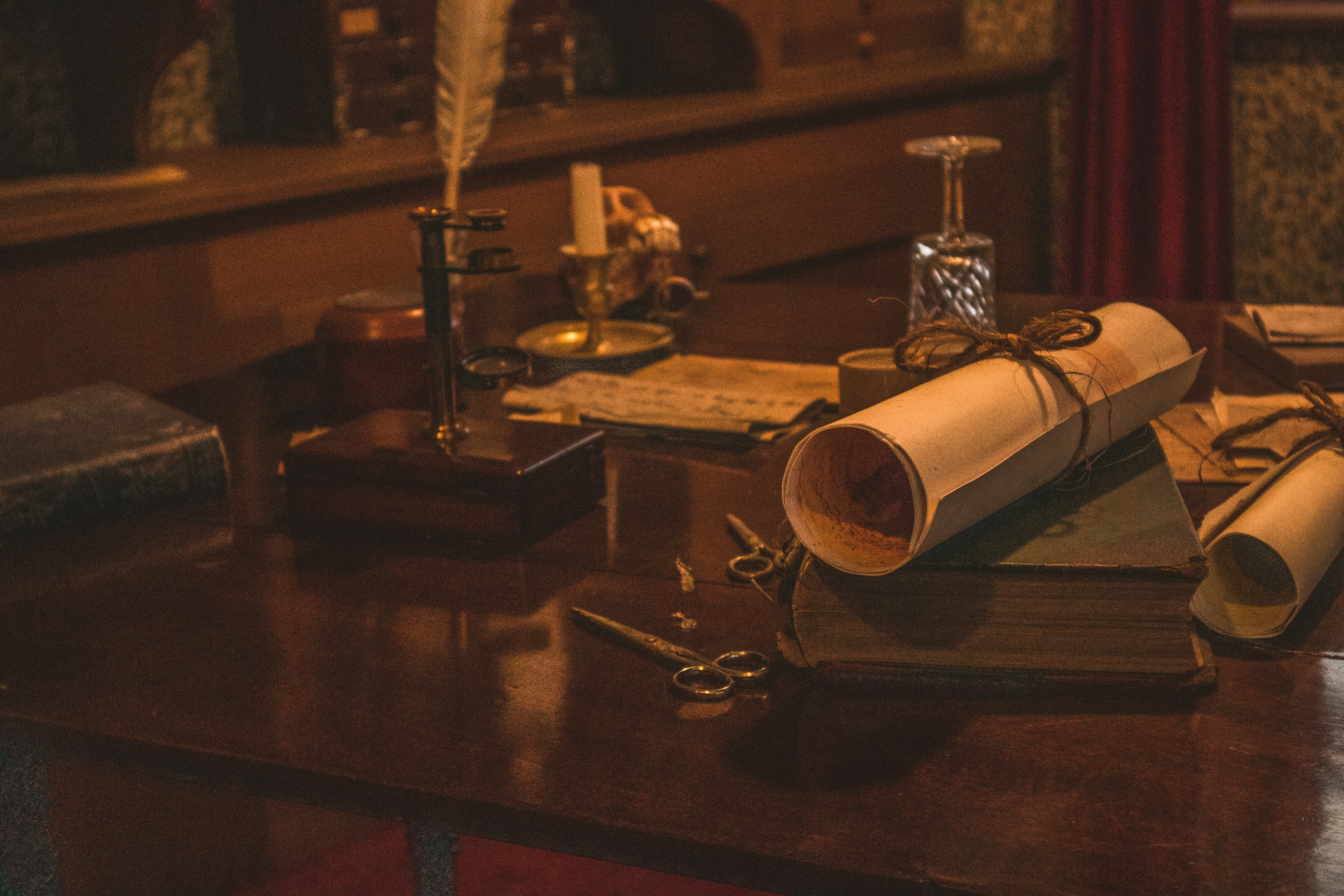 scissors beside rolled paper on book and feather pen on brown table