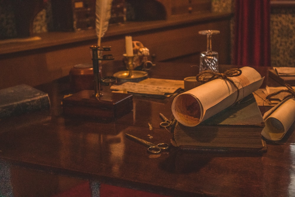 scissors beside rolled paper on book and feather pen on brown table