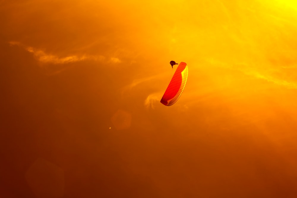 Person Gleitschirmfliegen unter orangefarbenem Himmel