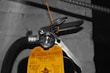 A close-up view of a fire extinguisher with a yellow inspection tag attached. The tag contains details about the service and inspection of the equipment. A pressure gauge is visible, indicating the operational status of the extinguisher. The background is a concrete wall with an electrical conduit running parallel to the extinguisher.