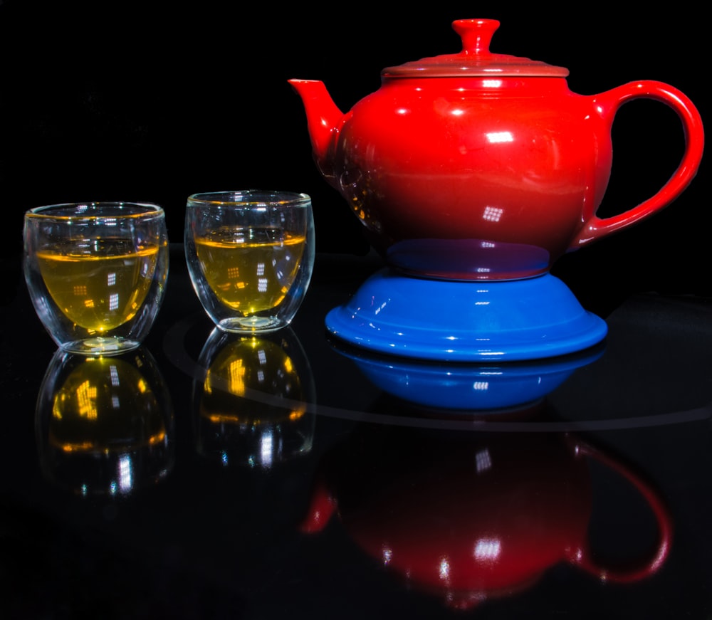 red teapot on blue container beside two clear glass teacups
