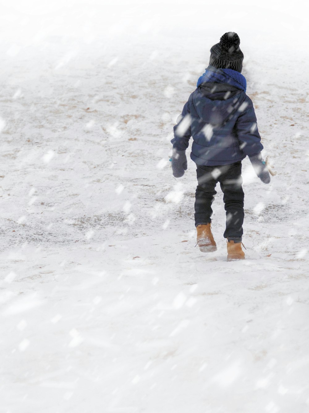 푸른 코트를 입은 아이가 눈밭을 걷고 있다.