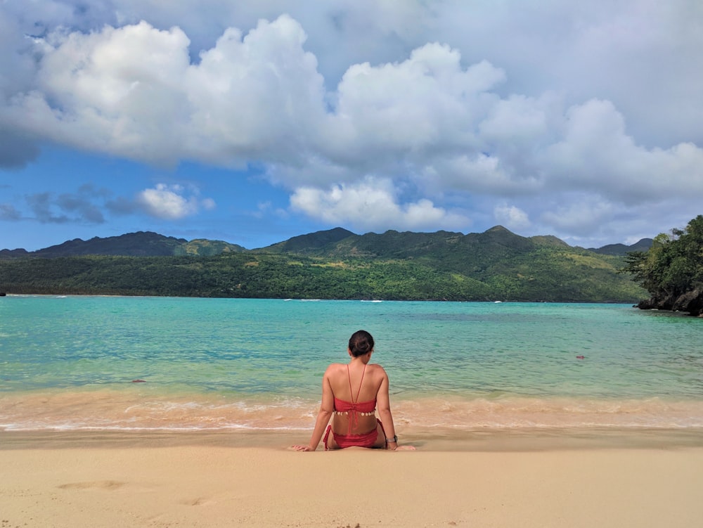 Mujer sentada cerca de la orilla del mar viendo el mar en calma