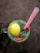 A refreshing beverage is presented in a glass mug on a wooden surface. The drink contains a whole lemon, small seeds dispersed throughout, and pieces of red peppers. A pink straw is placed in the mug, suggesting it is ready to be consumed.