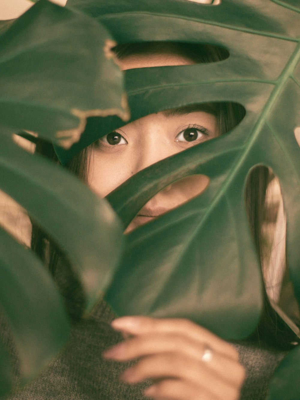 woman wearing silver-colored ring hiding behind green leaves