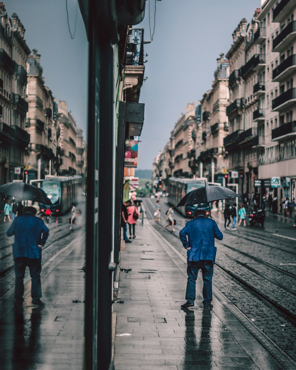 man holding black umbrella while walking on road during daytime