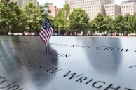 Close-up of a folded American flag resting on a memorial bench inscribed with a hero’s name.
