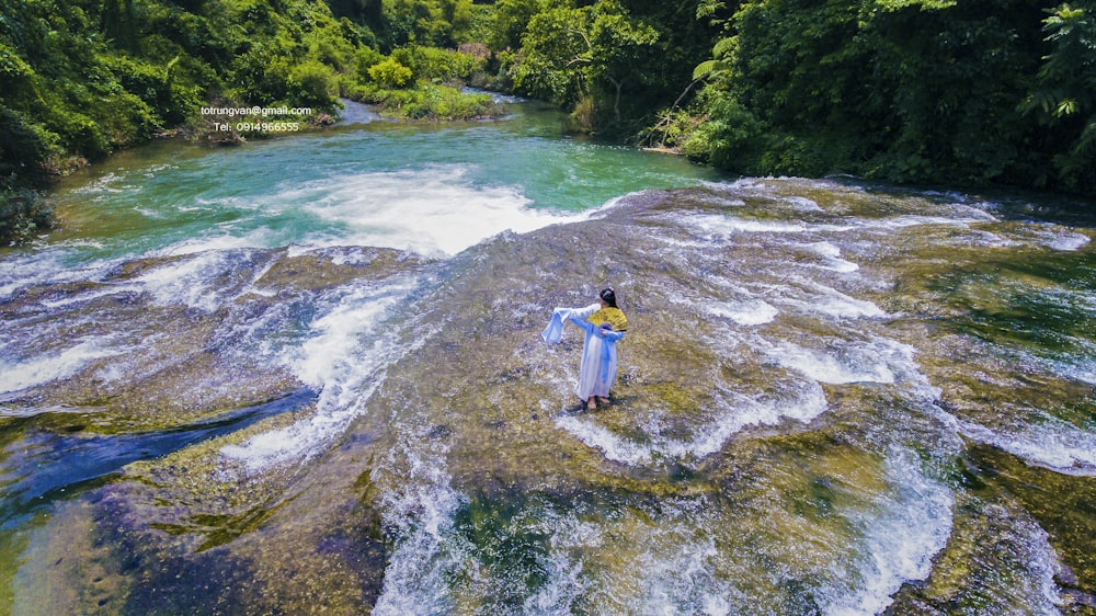 woman standing on river with rocks during daytime