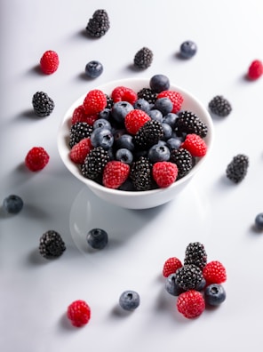 A cheerful toddler holding a bowl of colorful mixed berries.