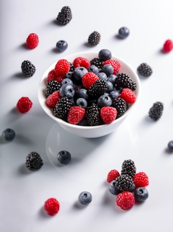 A bowl filled with assorted berries—blueberries, strawberries, and raspberries—on a wooden surface.