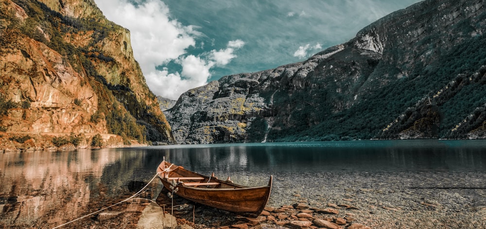 canoa de madeira marrom ao lado do rio e montanhas