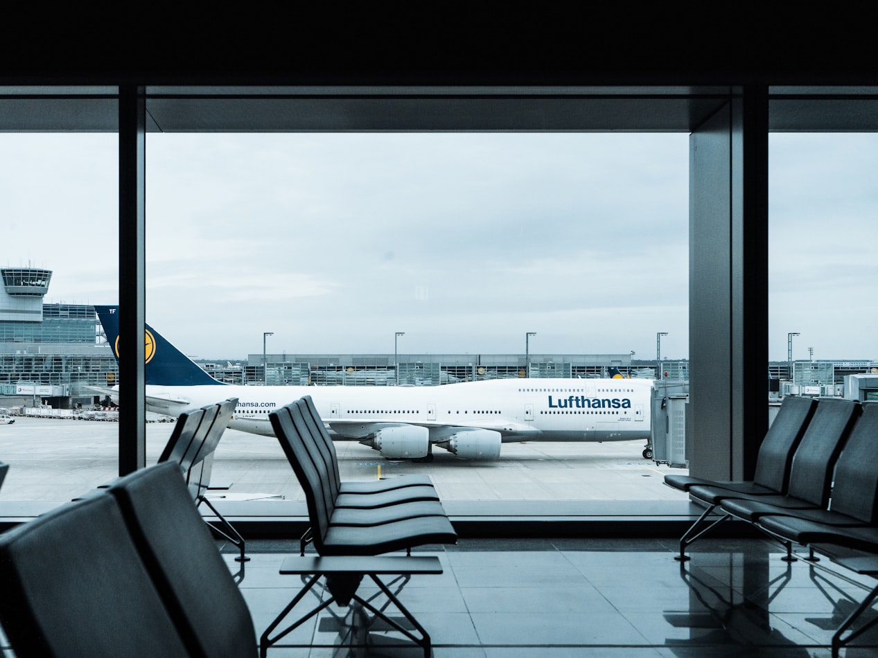 empty gray airport seats during daytime with an lufthansa aircraft in the background