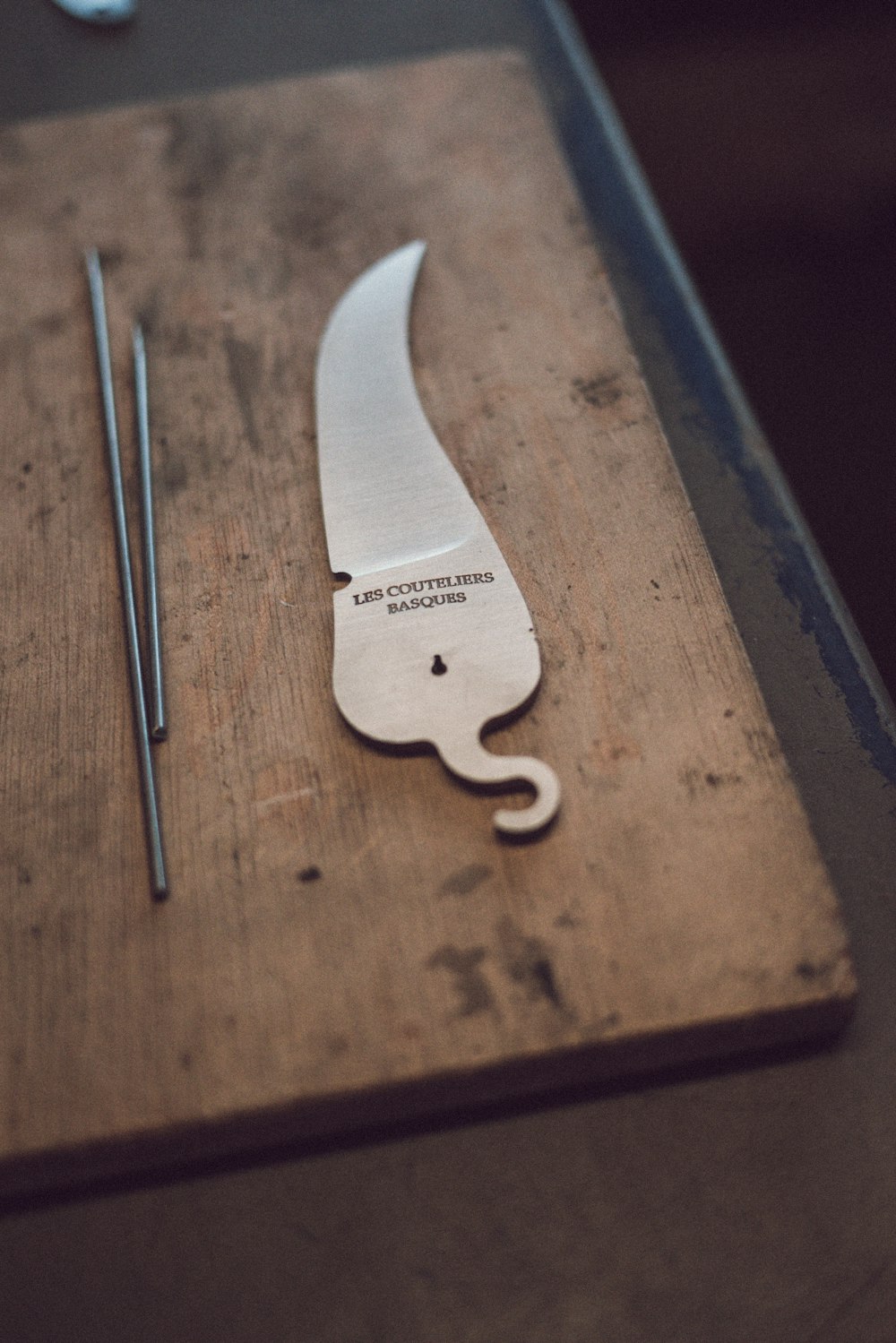 two grey metal sticks and hook like knife on wooden board